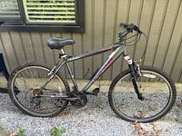 Side view of the Schwinn mountain bike against a beige wall, showing frame, tires, seat, and handlebar