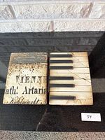 Photo of two Sid Dickens decorative resin tiles on black surface, showing vintage text tile and piano keyboard tile side by side.