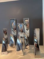 Front view of five twisted silver chrome decorative pillars of varying heights with reflective surfaces.