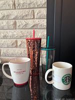 Photo of three Starbucks drinkware items with two ceramic mugs and one copper metallic tumbler with lids and straws.
