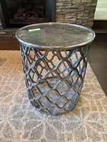 Full view of the small round steel end table with reflective metal top and open lattice base on carpet.