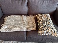 The throw blanket and decorative pillow lying side by side on a sofa, showing overall appearance and condition.