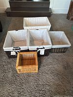 Five wicker baskets arranged together on carpeted floor showing different sizes and colors, three with liners and two without.