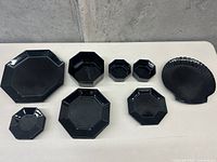 Top view of entire collection showing multiple octagonal black glass plates and bowls arranged with shell-shaped dish