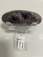 Side view of the 3.6 inch heart-shaped polished amethyst chevron stone on a clear stand with a price tag.