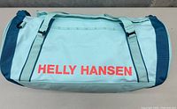 Front side of light blue Helly Hansen duffel bag showing the brand logo in red lettering.