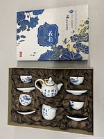 Set displayed inside its box with silk lining, showing teapot, creamer, six cups and six saucers with blue floral and calligraphy decoration.