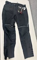 Photo showing front side of black motorcycle trousers with knee pads and reflective strips, tags attached.