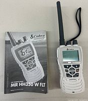 Front view of Cobra Marine handheld VHF radio MR HH350 W FLT with manual showing front buttons and screen display.