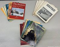 Two sets of vintage Canadian magazines displayed on a table: The Beaver issues with colorful front covers and Heritage issues with black-and-white front covers.