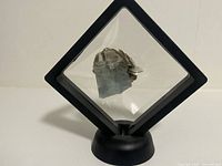 Front view of natural aquamarine with mica mineral specimen displayed in a black square frame stand on a flat surface.