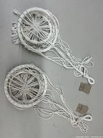 Two handmade white macramé plant pot hangers laid flat showing circular woven holders and long hanging cords with loops.