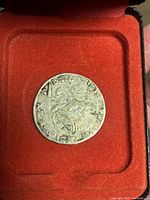 Front side of rare silver coin featuring a lion design, placed in red velvet-lined presentation case.