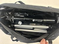 Open black carrying case showing Zhumell telescope tube, diagonal eyepiece, and tripod inside the case.