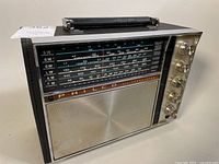 Side angled front view showing speaker grille, tuning scale, and control knobs with handle on top.