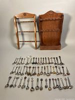 Overview showing two wooden display stands and over 60 assorted collector spoons laid out beneath them.