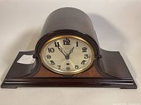 Front view of antique KIENZLE mantle clock showing curved wooden case and clock face with crystal door.