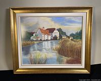 Framed pastel painting showing a landscape of houses by water with tall grass.