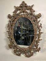 Full front view of the oval framed wall mirror showing the ornate carved frame and reflective glass surface.