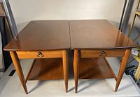 Front view of the pair of walnut Mersman end tables side by side showing tops and lower shelves.