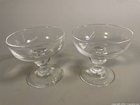 Pair of clear Steuben crystal champagne coupe glasses on neutral background, showing overall shape with wide bowl and baluster stem.