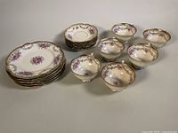 All dessert plates, teacups, and saucers arranged on a flat surface showing floral and gold trim details