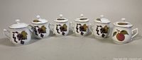Front view of six Royal Worcester porcelain cream cups with lids featuring grape and plum fruit designs.