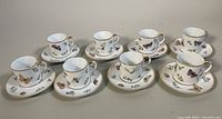 Photo of all eight demitasse teacup and saucer pairs arranged in two rows, decorated with butterfly and floral designs and gold trim.