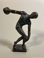 Front and side view of dark metal Discobolus sculpture showing detailed musculature and discus in hand.