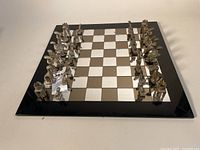Full view of the complete chess set on the board showing mirrored squares and metal pieces arranged ready for play.