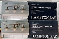 Two boxed Hampton Bay Glenhurst 3-light vanity fixtures stacked, showing front packaging with product image and brand.