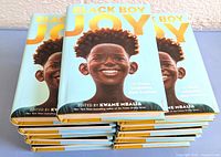 Photo showing a stack of 11 hardcover books titled 'Black Boy Joy' with a blue cover and illustration of a smiling Black boy.