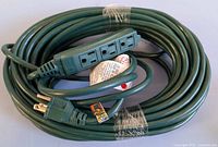 View of the green extension cord coiled with three grounded outlets visible, alongside a grounded plug, label attached.