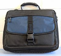 Front view of the Targus laptop bag showing black and blue external fabric, front zipper pocket, buckle clasp, and top handle with rubber grip.