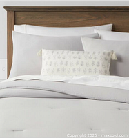 Image of made bed with queen comforter, two standard shams, and a floral print oblong pillow arranged on wooden headboard bed