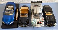 Top-down view of four diecast model cars showing colors, scale, and detail arrangement from left to right: blue Jaguar XK8 Convertible, black BMW 502, silver Mercedes-Benz CLK-GTR racing car, and black Jaguar E coupe.