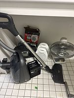 Overview showing grey canister vacuum, black Super Furnace heater, boombox, two white heaters and silver fan grill