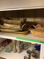 Shelf containing stacked bamboo trays, wooden tray with lid, and pottery serving trays.