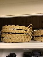 Three woven bamboo trays/baskets stacked on white shelf, showing braided woven design and handles
