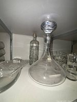 Clear glass decanter with stopper alongside textured glass bottle and clear glass bowls