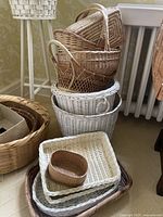 Various woven baskets and trays stacked, showing different styles and colors, including natural and white finishes.
