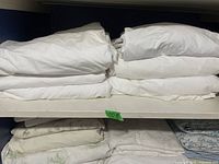 Stack of folded white bedsheets and duvet covers with minor marks, stored on shelf.