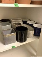 Shelf displaying multiple ceramic vases of varied colors and shapes including black, white, blue, gray, and beige.