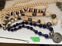 Close-up of four beaded necklaces: white, black and white striped, cream with silver beads, and blue with silver medallion pendant.