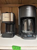 Two coffee makers side by side on a shelf, one KRUPS and one Elite Gourmet.