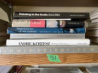 Stack of seven large hardcover photography and art coffee table books arranged on a wooden shelf, show titles and varied spine designs.