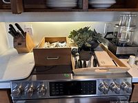 Kitchen counter with wooden knife block, wooden drawer with spoons, and utensils with food processor on counter.