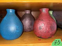 Five glass bottles with speckled finish and three clear rectangular glass trays on a wooden shelf.