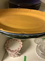 Large yellow serving plate stacked over other plates including purple ones and some smaller pink scalloped dishes below.