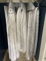 Multiple white duvet covers and quilt hanging in a closet, all stored in protective plastic garment bags.